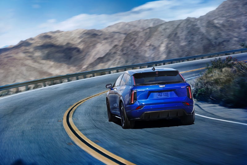 Rear View of a Blue 2026 OPTIQ-V Driving on a Curve of a Mountain Row | Bob Johnson Cadillac in ROCHESTER NY